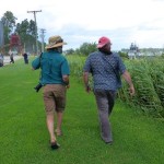 Two men walking in grassy field by river.