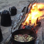 Campfire cooking with pots and fire.