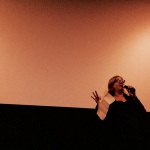 Woman speaking into microphone on stage.