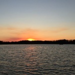 Sunset over a calm lake with trees in the distance.