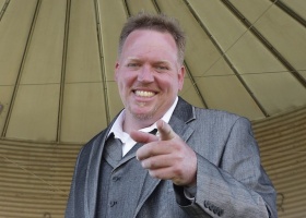 Man in suit smiling and pointing.