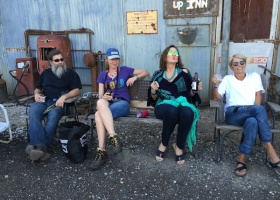 Four people sitting on a porch with drinks.