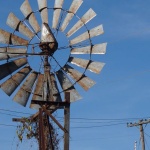 Rusty windmill with vines under blue sky.