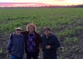 Three men standing in a field at sunset.