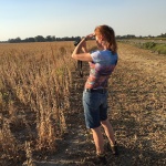 Woman in a field using binoculars.