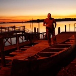 Man standing on dock with canoe at sunset.