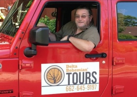 A man in a red Jeep with Delta Bohemian Tours logo.