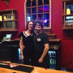 Couple posing at a bar with drinks behind them.