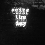 Neon sign saying "Seize the day" on brick wall.