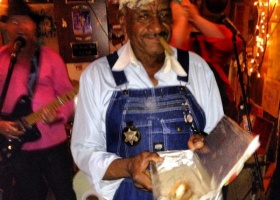 Man in overalls holding a box with a cigar in his mouth.