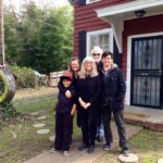 Family standing outside a red house with a swing.