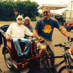 Three people riding a red tricycle and a bike.