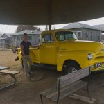 Man standing next to yellow 1954 pickup truck.