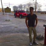 Man in sunglasses standing by a red jeep.