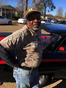 Man in camo shirt leaning on a car.