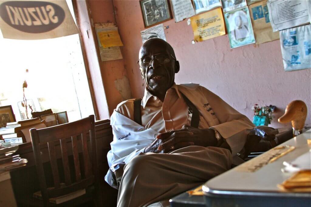 An elderly man sits at a desk.