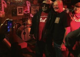 Three men posing for a photo with a drum set.