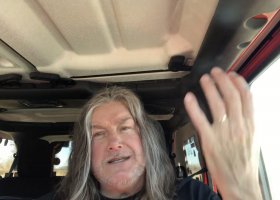 Man with long hair talking in a car.