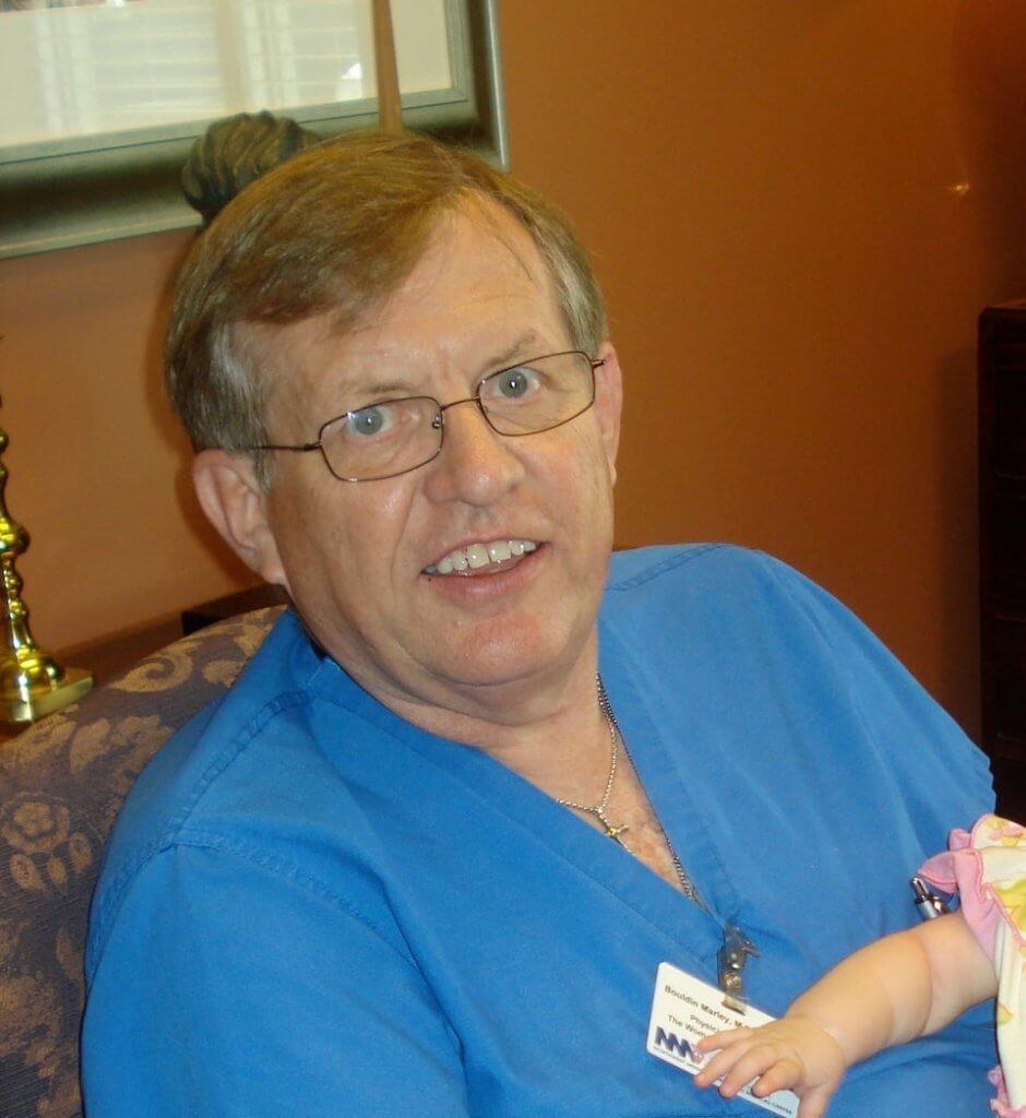 Man in blue scrubs holding a baby.