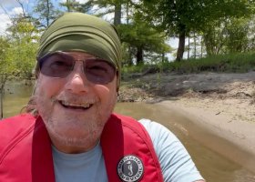 Man smiles in a red life vest on a boat.