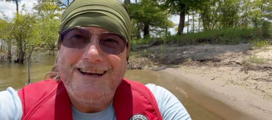 Man smiles in a red life vest on a boat.