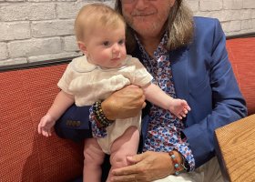 Man in hat holds baby on couch.