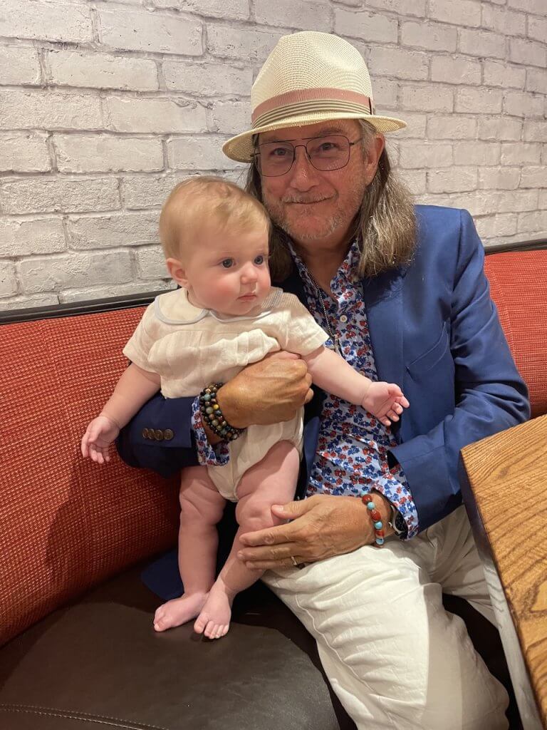 Man in hat holds baby on couch.