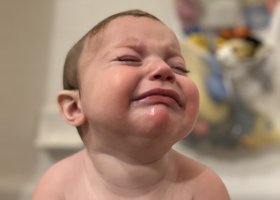 A baby with wet hair crying in the tub.