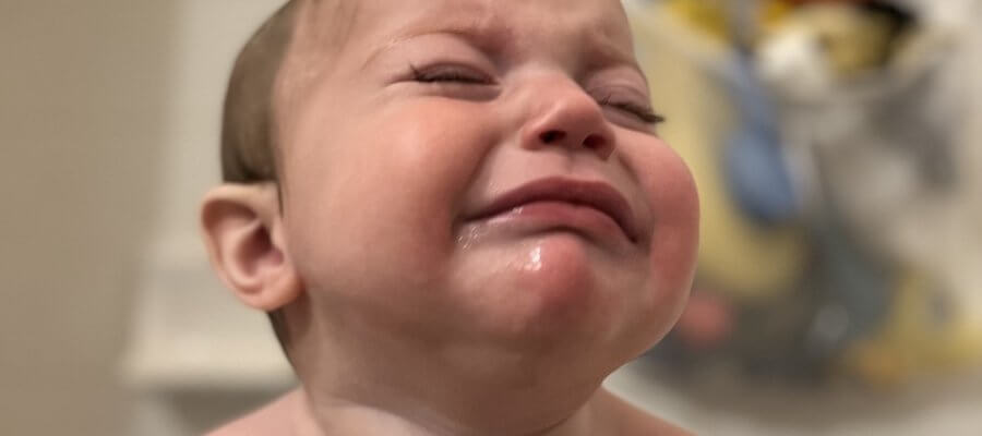 A baby with wet hair crying in the tub.