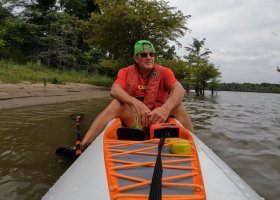 Man kayaking on a lake with trees in the background.