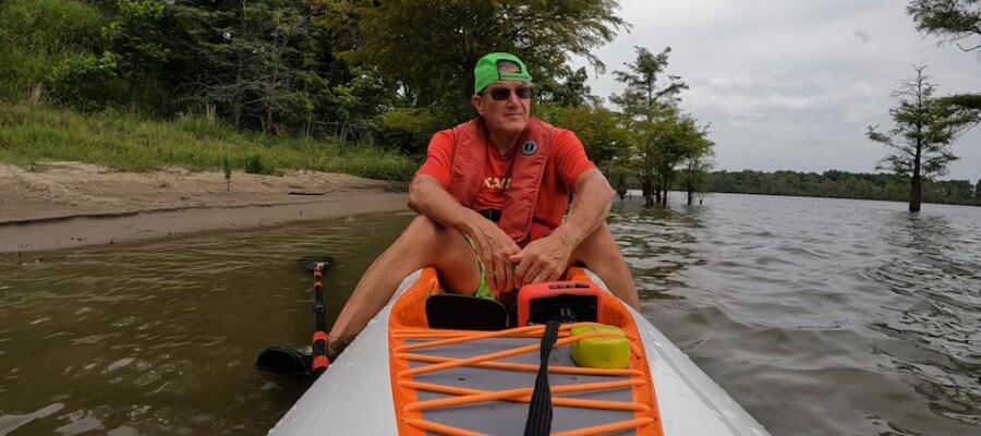 Man kayaking on a lake with trees in the background.