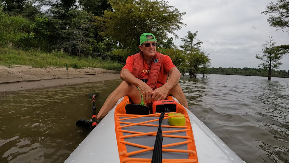 Man kayaking on a lake with trees in the background.