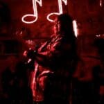 Person playing guitar in a red lit room.
