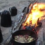 Campfire cooking with pots and fire.