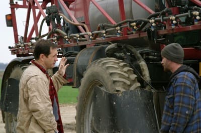 Farmers talking beside large tractor wheels
