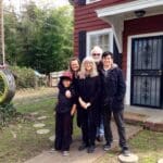 Family standing outside a red house with a swing.
