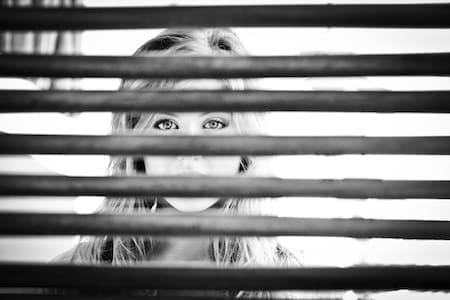 Girl peering through window blinds.