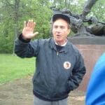 Man in blue jacket gesturing near statue.