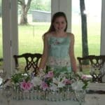 Young girl in blue dress at table with flowers.