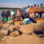 Group of people on riverbank with canoe.
