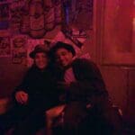 Two men in hats sit in red lit room.
