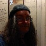 A man with long hair and glasses in a bathroom.