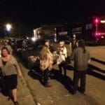 People gathered by a tour bus at night.