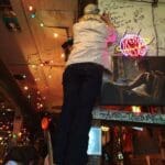 Man in a bar writing on a wall.