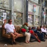 People sitting and standing outside a store.