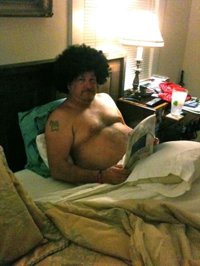 Shirtless man with afro wig in bedroom