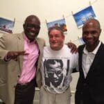 Three men smiling, one in a pink shirt.