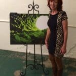 Woman standing next to an easel and artwork.