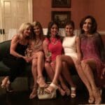 Five women smiling on a couch.