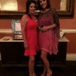 Two women in formal wear smiling at a party.